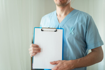 Close up of young man healthcare worker with blue satin ribbon and empty clipboard sheet. Horizontal Banner for November prostate cancer awareness, prevention, and medical diagnostics concept.