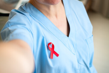 Woman medical professional taking phone selfie with red ribbon on uniform, showing support and solidarity in HIV AIDS awareness movement.