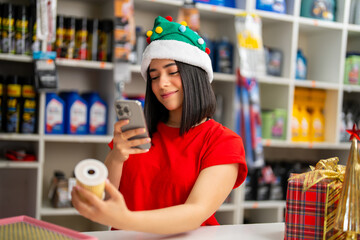 Woman wearing a christmas hat scanning an auto part with her smartphone in a store