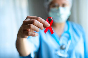 Doctor in medical uniform holds in hand red satin awareness ribbon, symbolizing HIV AIDS solidarity, support and hope for future treatment.