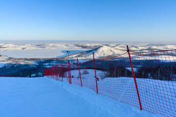 Steep ski slope at sunset against the backdrop of the picturesque landscape of the Ural Mountains.
