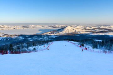 Steep ski slope at sunset against the backdrop of the picturesque landscape of the Ural Mountains.