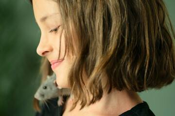 Profile view of a happy laughing child with her gray dusty pet rat sitting on her shoulder. Close up shot showing joy, friendship and love for small animals.
