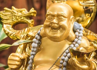 Close up of a golden Laughing Buddha statue (Budai or Hotei) holding a gold ingot. Figure symbolizes wealth, happiness, and good fortune in Feng Shui and Buddhism.