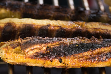 Close up of ripe plantains roasting on a hot metal barbecue grill. The skin is charred and caramelized. Traditional street food or side dish preparation from the Amazon.