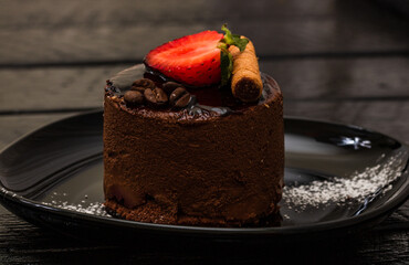Chocolate mousse with strawberry and chocolate stick on a black dish.