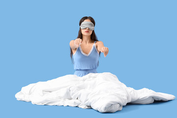 Naklejka premium Female sleepwalker in pajamas with blanket sitting on blue background