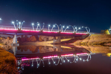 Illuminated bridge at night reflecting on calm water with vibrant colors and serene atmosphere