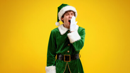 Festive man yawning in a vibrant elf costume against a bright yellow background during holiday season preparations
