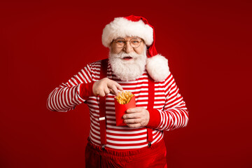 Santa in striped outfit enjoys fries in red winter background for Christmas themed advertising and promo imagery