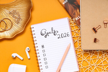 Notebook with 2026 goals, earphones and accessories on orange background