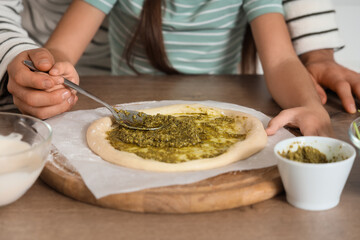 Father with his daughter applying pesto sauce to pizza dough in kitchen, closeup