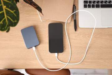 Power bank and mobile phone with charging cables on desk in office, top view