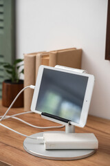 Tablet computer charging from power bank on shelf in room, closeup