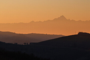 Stunning evening sunset over Piedmont's Langhe and Asti region, with the majestic snow-capped Monte Rosa and Alps glowing in warm alpenglow against a dramatic pink-orange sky. Perfect panoramic vista 