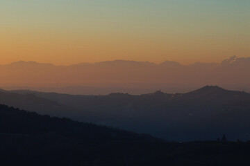 Stunning evening sunset over Piedmont's Langhe and Asti region, with the majestic snow-capped Monte Rosa and Alps glowing in warm alpenglow against a dramatic pink-orange sky. Perfect panoramic vista 