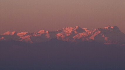 Stunning evening sunset over Piedmont's Langhe and Asti region, with the majestic snow-capped Monte Rosa and Alps glowing in warm alpenglow against a dramatic pink-orange sky. Perfect panoramic vista 