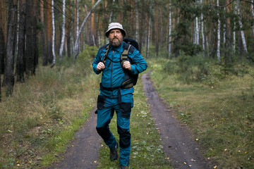 A man in a blue jacket and blue trousers walks along a dirt road