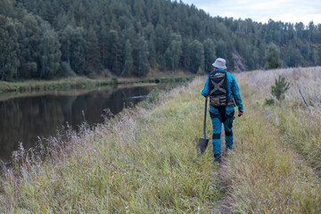 Obraz premium A man with a backpack and a shovel walks along the river