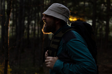 A man with a beard and a hat is walking through a forest