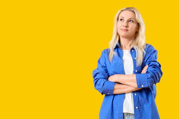 Thoughtful mature blonde woman on yellow background