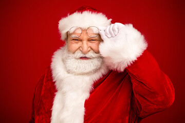 Santa in traditional red suit with white fur trim adjusts glasses in a bright studio setting for a festive holiday portrait