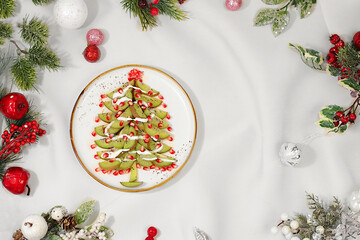 Winter background for greeting card. Edible Christmas tree made of kiwi and pomegranate on the...