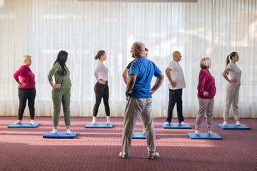 Fototapeta premium Instructor leading a diverse group of people during a fitness training session with stretching exercises on mats in a bright wellness center