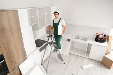 Male worker assembling cupboard on stepladder in kitchen
