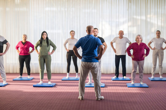 Instructor leading a diverse group of people during a fitness training session with stretching exercises on mats in a bright wellness center - Powered by Adobe