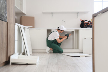 Male worker with drill assembling furniture in kitchen