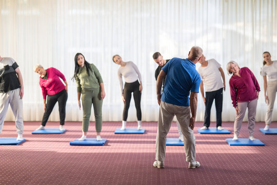 Instructor leading a diverse group of people during a fitness training session with stretching exercises on mats in a bright wellness center