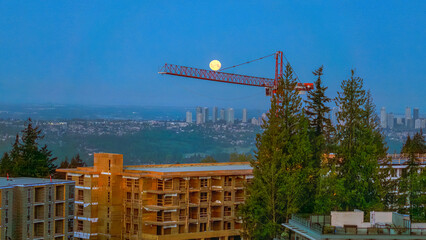 Full moon seemingly balanced on a construction crane as viewed from Burnaby Mountain, BC, Canada.