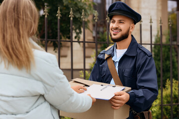 Handsome postman delivering parcel to woman on street