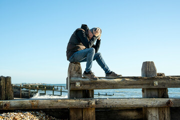man sitting by the ocean with his head in his hands