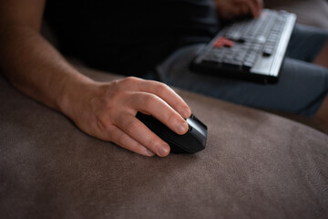 Close-up of a person using a wireless computer mouse on a sofa while holding a keyboard. Cozy remote work, gaming, or home office concept with modern technology and relaxed atmosphere