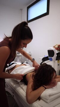 Professional beautician placing applicators from a body contouring machine on a female client's back and waist, preparing for a non invasive fat reduction and muscle toning procedure