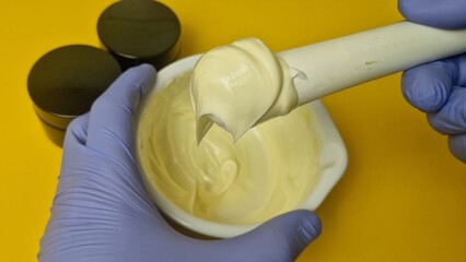 Extreme close-up view of a cosmetic chemist mixing a luxurious, yellow cream base in a white...