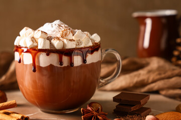 Glass cup of hot cocoa drink with whipped cream and marshmallows on beige table