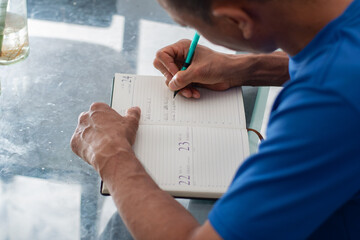 Close detail of left hand holding pen writing in notebook on glass table, amputated four fingers visible