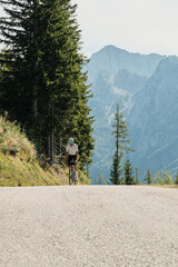 Man cycling uphill on a scenic mountain road with majestic peaks and lush green trees. Focused on fitness, adventure, and the beauty of nature. Healthy lifestyle, freedom.