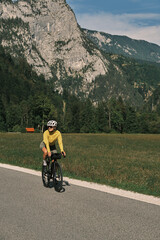 Woman cycling on a scenic mountain road.  Athlete training outdoors, enjoying beautiful nature.  Road cycling on a sunny day, promoting a healthy lifestyle and fitness.