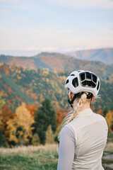 Woman in cycling helmet looking at scenic autumn mountain landscape. Rear view of cyclist taking break, enjoying nature and outdoors. Sport, recreation and active lifestyle concept.