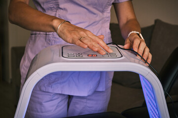Woman operates light therapy device, focusing on health and wellness.  Ideal for illustrating skincare, dermatology, pain relief, and alternative medicine concepts with modern equipment. 