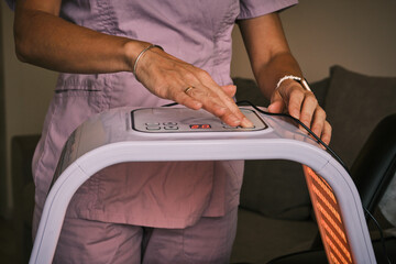 Close up of a woman adjusting settings on a red light therapy device. Promoting wellness, pain relief, and skin rejuvenation with light therapy technology. Modern home healthcare.