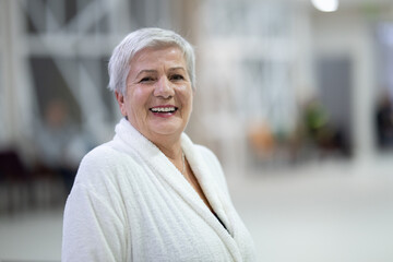 Portrait of a senior woman wearing a white bathrobe at a wellness center, symbolizing relaxation, self-care, and healthy aging lifestyle.