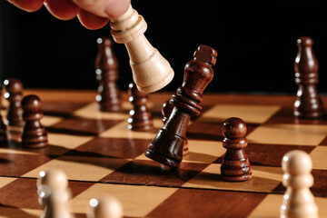A hand delivers the final capture as a white piece knocks over the dark king—decisive endgame...