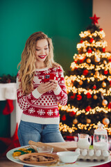 Playful christmas scene with a smiling blonde woman in a red white sweater by a lit christmas tree...