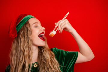 Festive young woman dressed as an elf enjoying sushi with smiling happy expression against a...