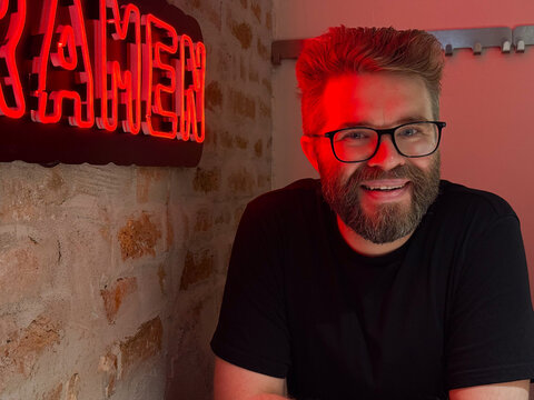 Man smiling in cafe with red neon light. Urban communication, modern lifestyle, and cheerful social interaction.
